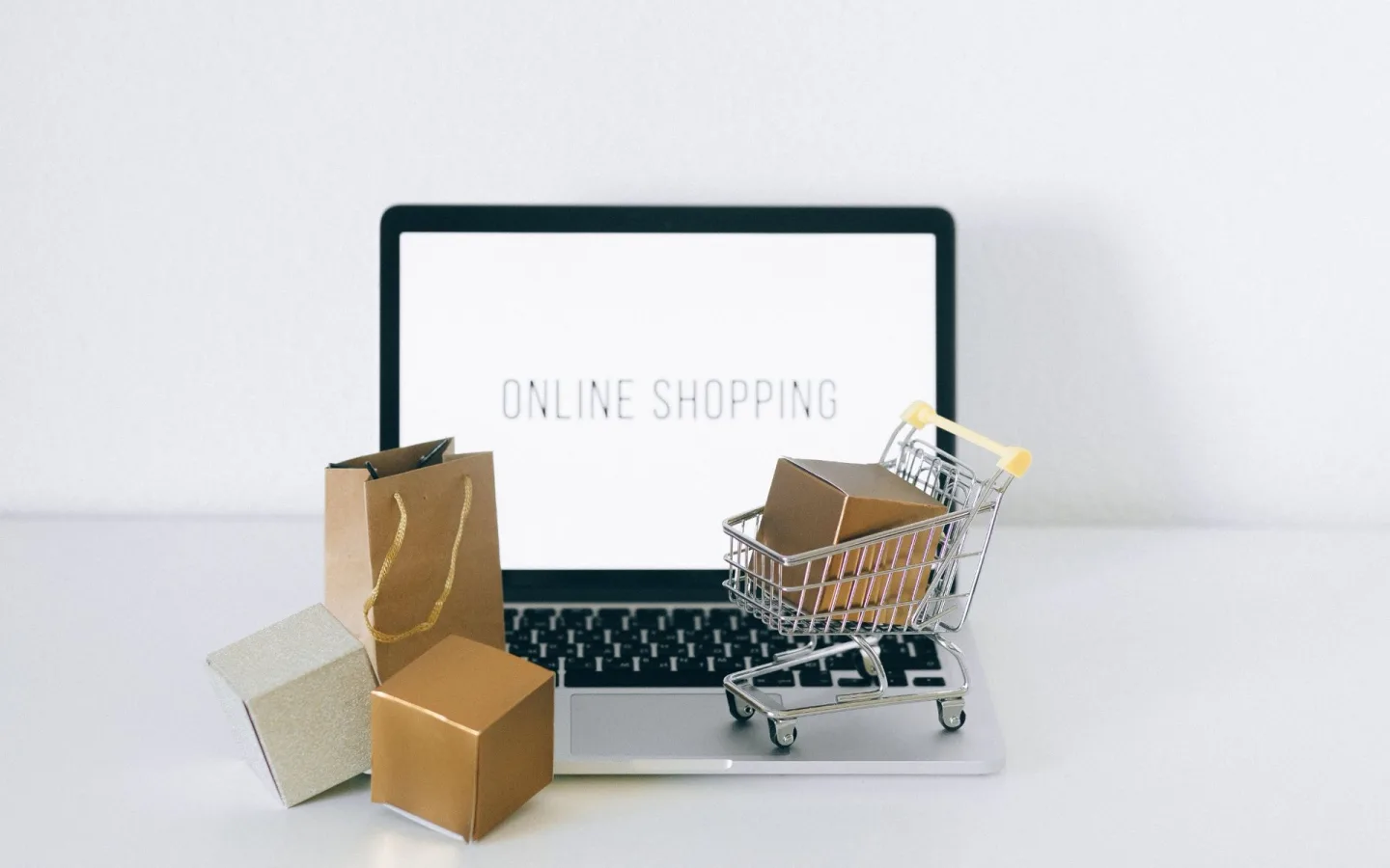 Computador portátil com carrinho de compras e pequenas embalagens, representando uma loja online.