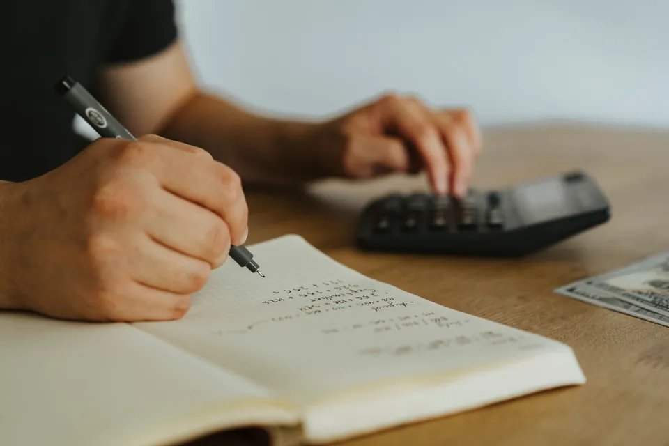 Profissional a registar cálculos junto a uma calculadora, representando organização de informação e trabalho contabilístico